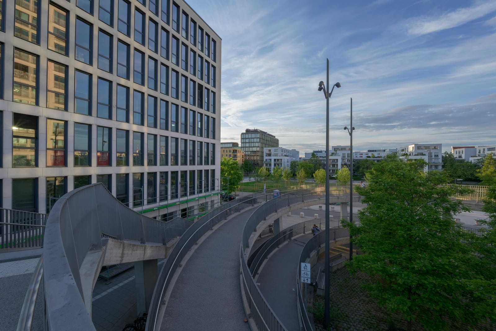 Curving pedestrian ramps beside a glass office building under evening clouds.
