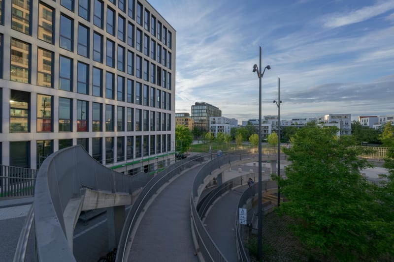 Curving pedestrian ramps beside a glass office building under evening clouds.