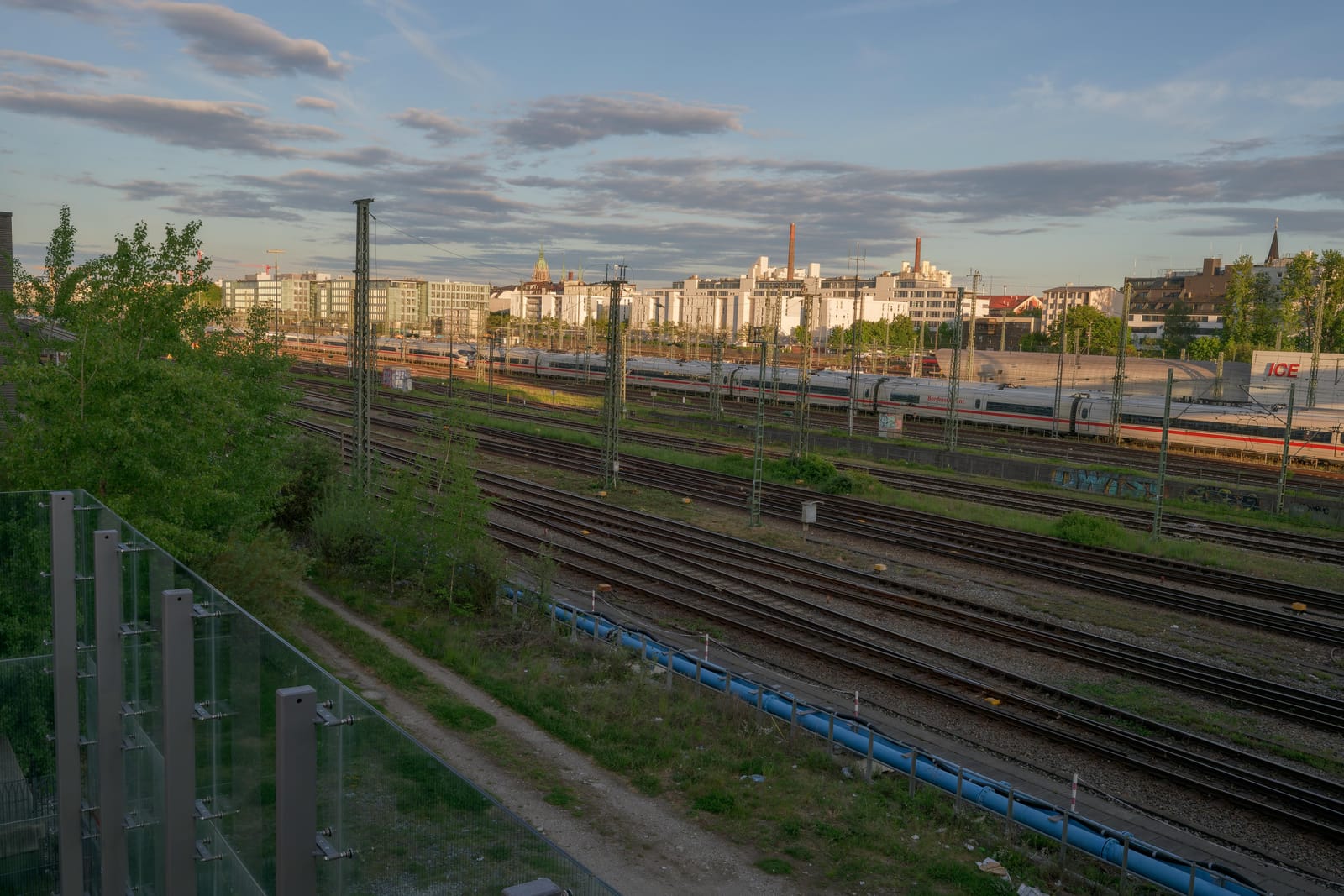 Rail yard tracks leading toward the Munich skyline at golden hour.