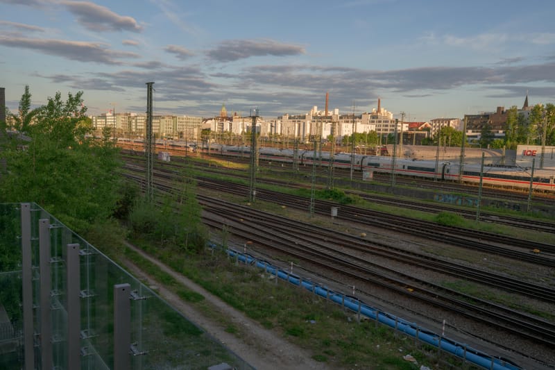 Rail yard tracks leading toward the Munich skyline at golden hour.