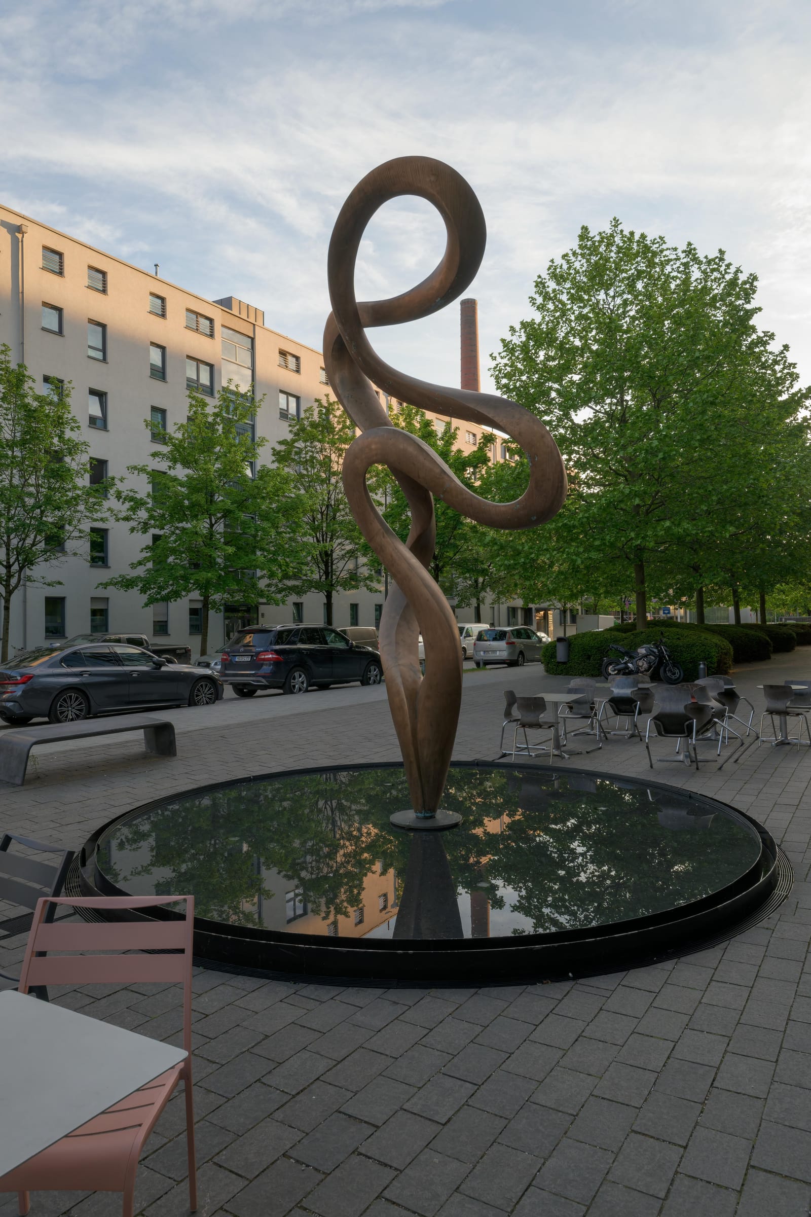 Looping bronze sculpture standing in a dark round fountain on a plaza.